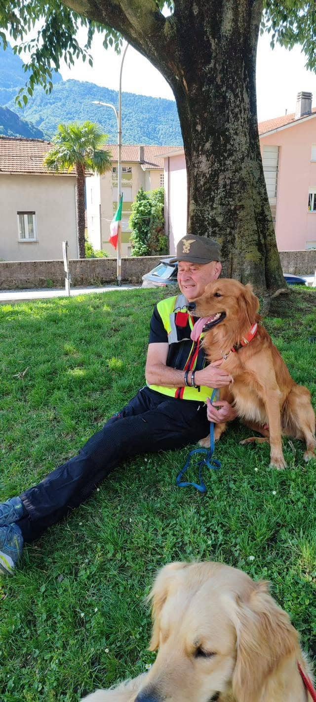 Istruttore cinofilo in pettorina alta visibilità abbraccia un Golden Retriever sull'erba