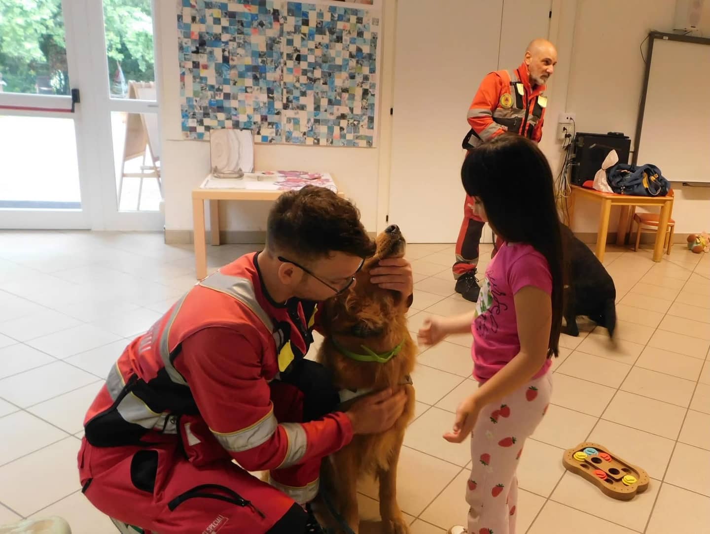 Volontario di Croce Rossa accarezza un cane davanti a una bambina