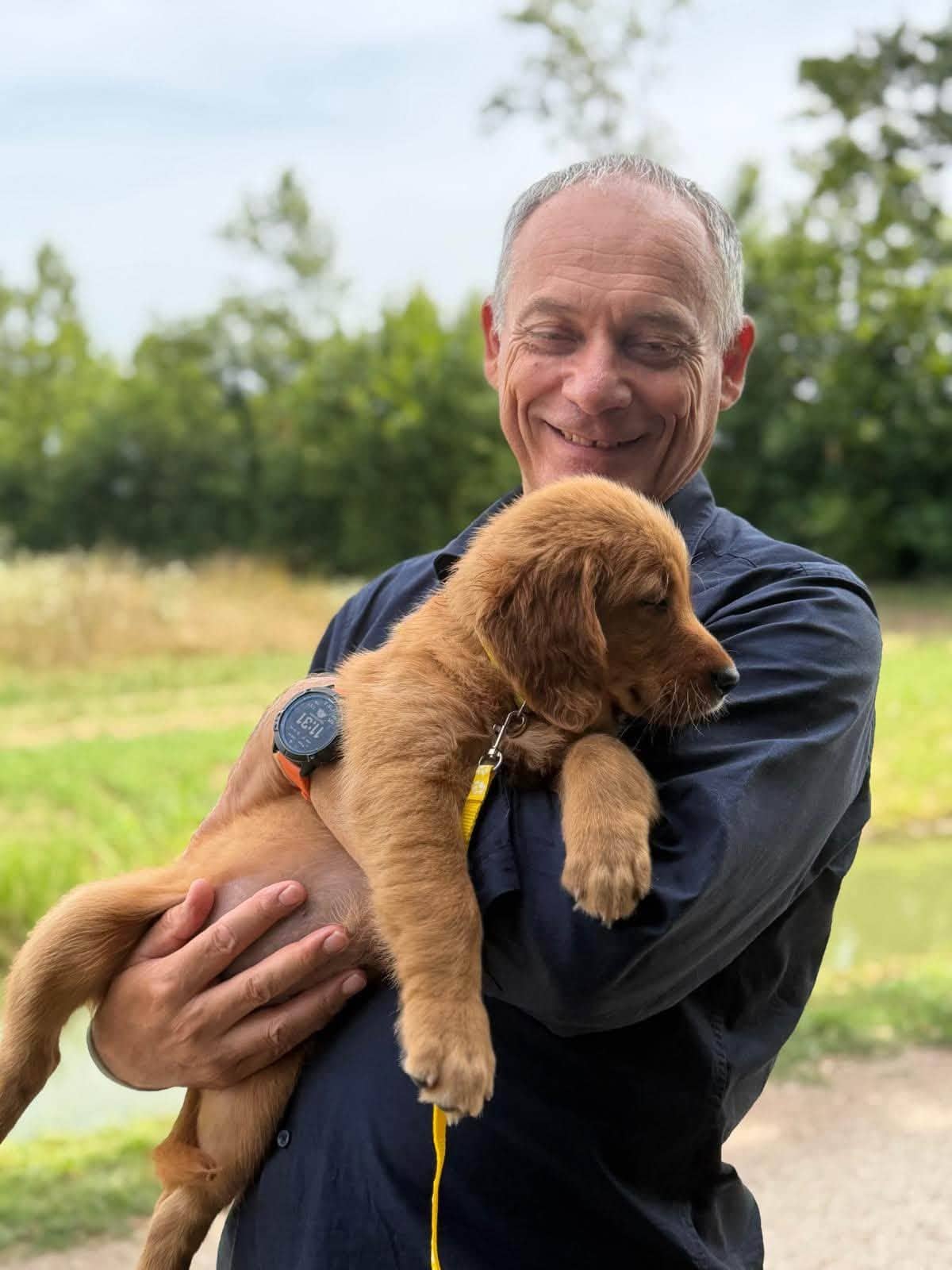 Uomo tiene in braccio un cucciolo di Golden Retriever vicino a uno stagno